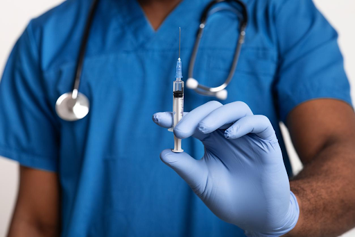 Healthcare professional in blue scrubs and gloves holding a syringe, preparing for vaccination."