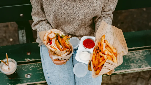 A person sitting outdoors holding fast-food items, including fries and a wrapped sandwich, symbolizing unhealthy dietary habits linked to rising colorectal and gastrointestinal cancer risks.