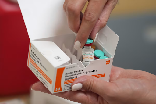A healthcare professional opens a box containing a Shingrix shingles vaccine vial, preparing it for administration in a clinical setting.